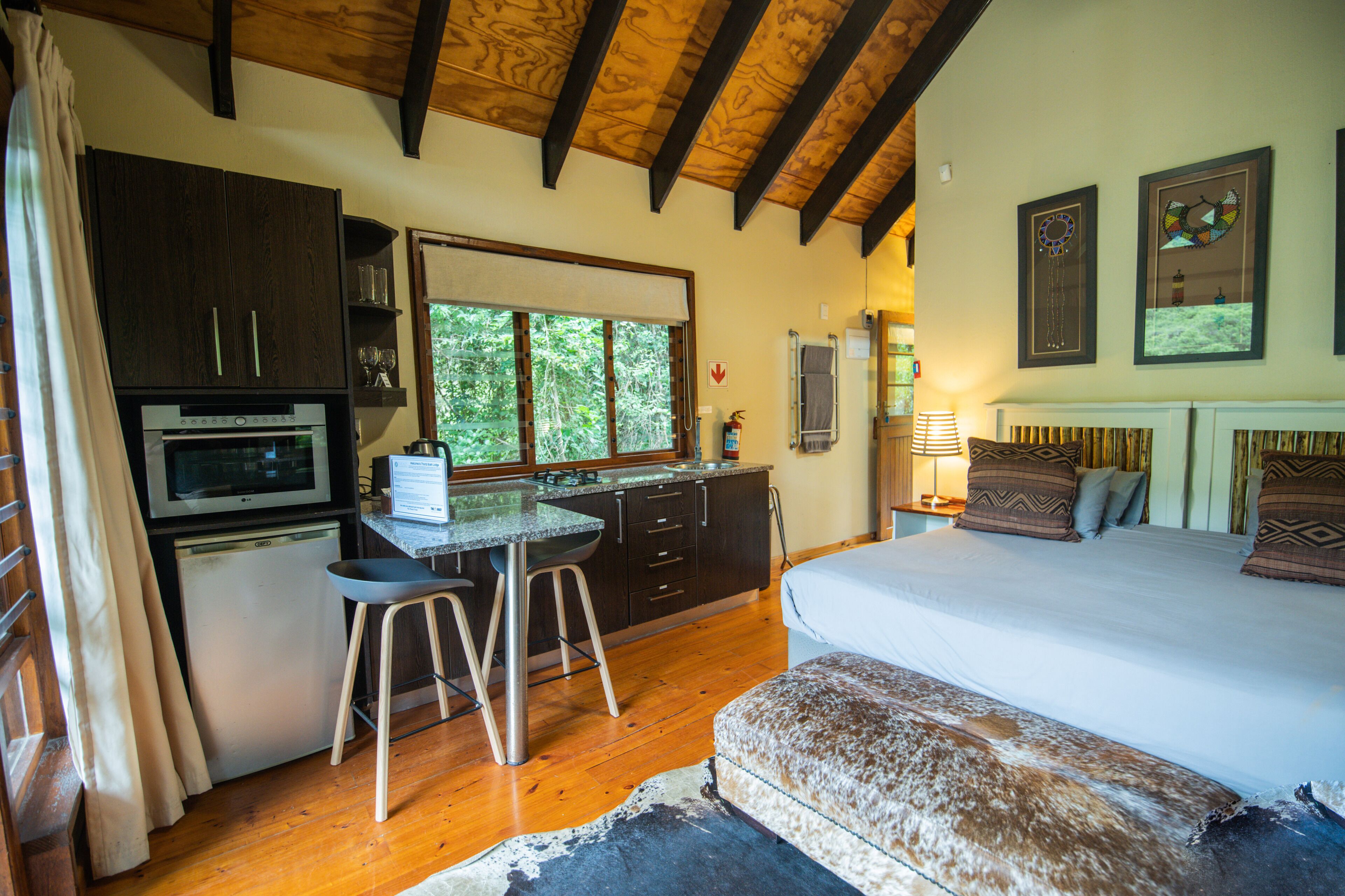 A compact bedroom with a bed, a small kitchenette, and a window.