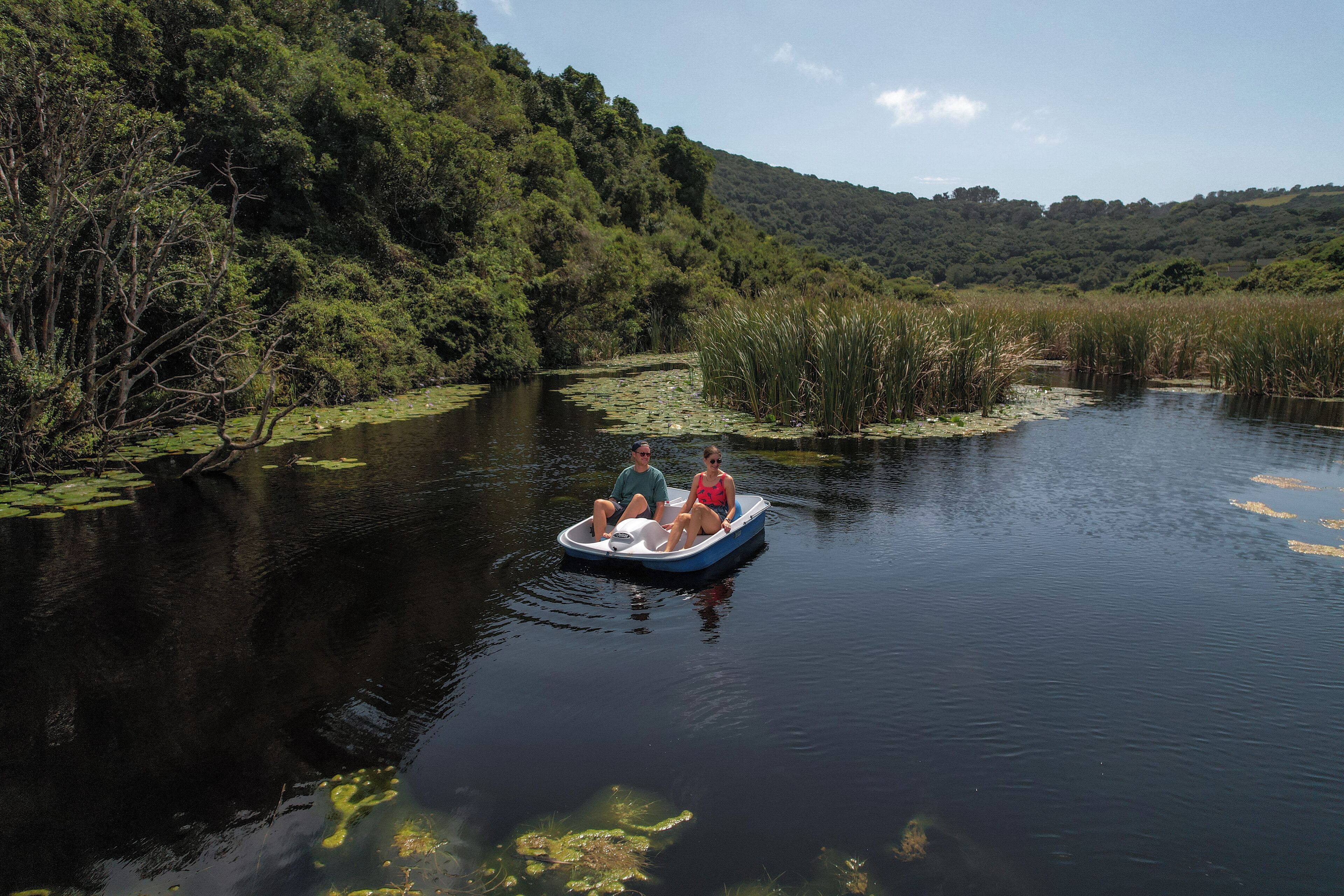 Un couple est dans un petit bateau sur une rivière paisible, entouré d’une végétation luxuriante.