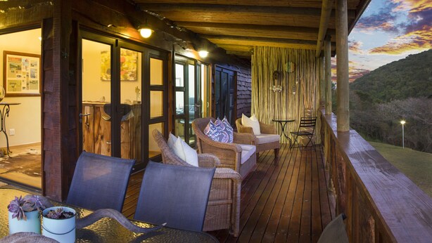A wooden deck with outdoor seating, including wicker chairs and a table, overlooking a scenic landscape. - Thunzi Bush Lodge (Gqeberha (Port Elizabeth))