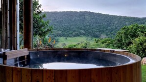 A hot tub with a wooden exterior, surrounded by lush greenery and a mountainous backdrop. - Thunzi Bush Lodge (Gqeberha (Port Elizabeth))