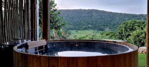 Relax in a serene hot tub with a panoramic view of the lush valley and forested hill.