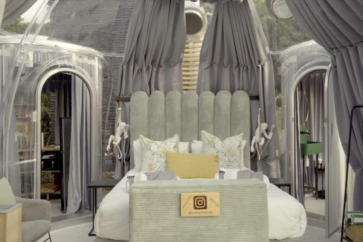 A spacious bedroom with a large bed, grey curtains, and a view of the outdoors.