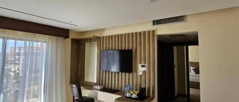 A hotel room with a bed, a desk, a chair, a TV, and a view of the city through the window.