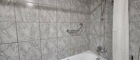 A bathroom with a bathtub, a shower, and a handrail.