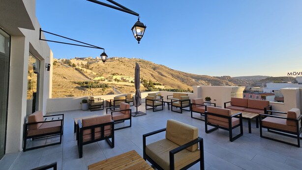 A rooftop terrace with outdoor seating, a view of a hilly landscape, and a clear sky. - Edom Hotel (Wadi Musa)