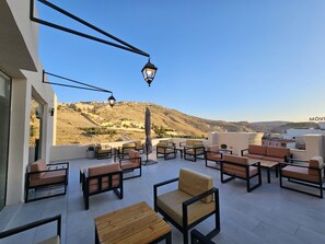 Una terraza en la azotea con mobiliario exterior, vista a un paisaje montañoso y cielo despejado.