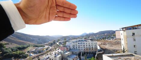 A hand over a view of a town with buildings and a mountainous background.