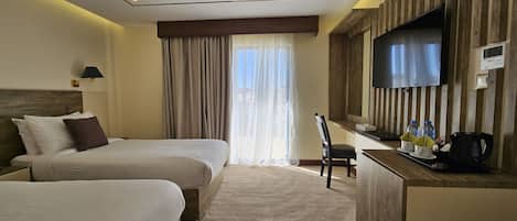 A hotel room with two beds, a desk with a flat-screen TV, a coffee maker, and a window with curtains.
