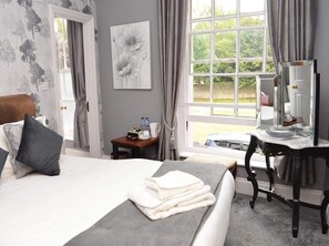 A hotel room with a large bed, a desk, a mirror, and a window with a view of greenery.