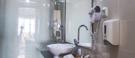 A modern bathroom with a glass-enclosed shower, a sink with a mirror, a hairdryer, and a soap dispenser.