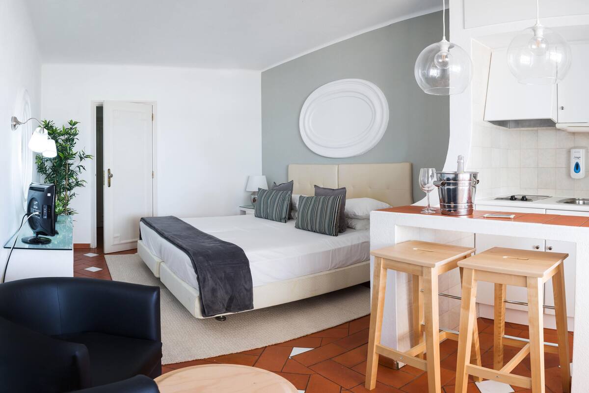 Une chambre d’hôtel de taille réduite, comprenant un lit, une table de chevet et une petite kitchenette.