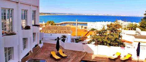 Un área de piscina en la azotea con sillones de descanso y vistas al mar.