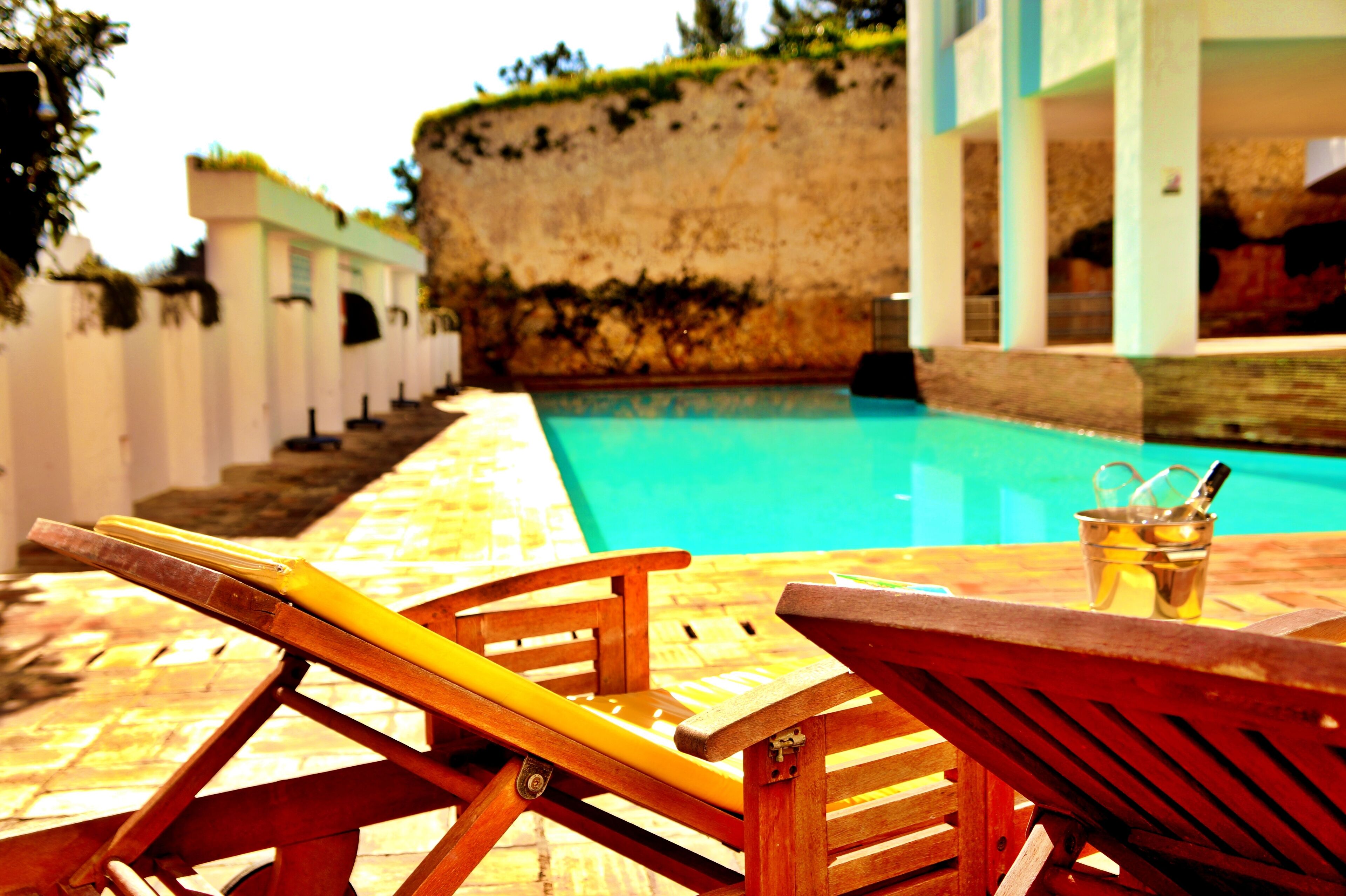 Area piscina con poltrona prendisole in legno e piscina cristallina blu.