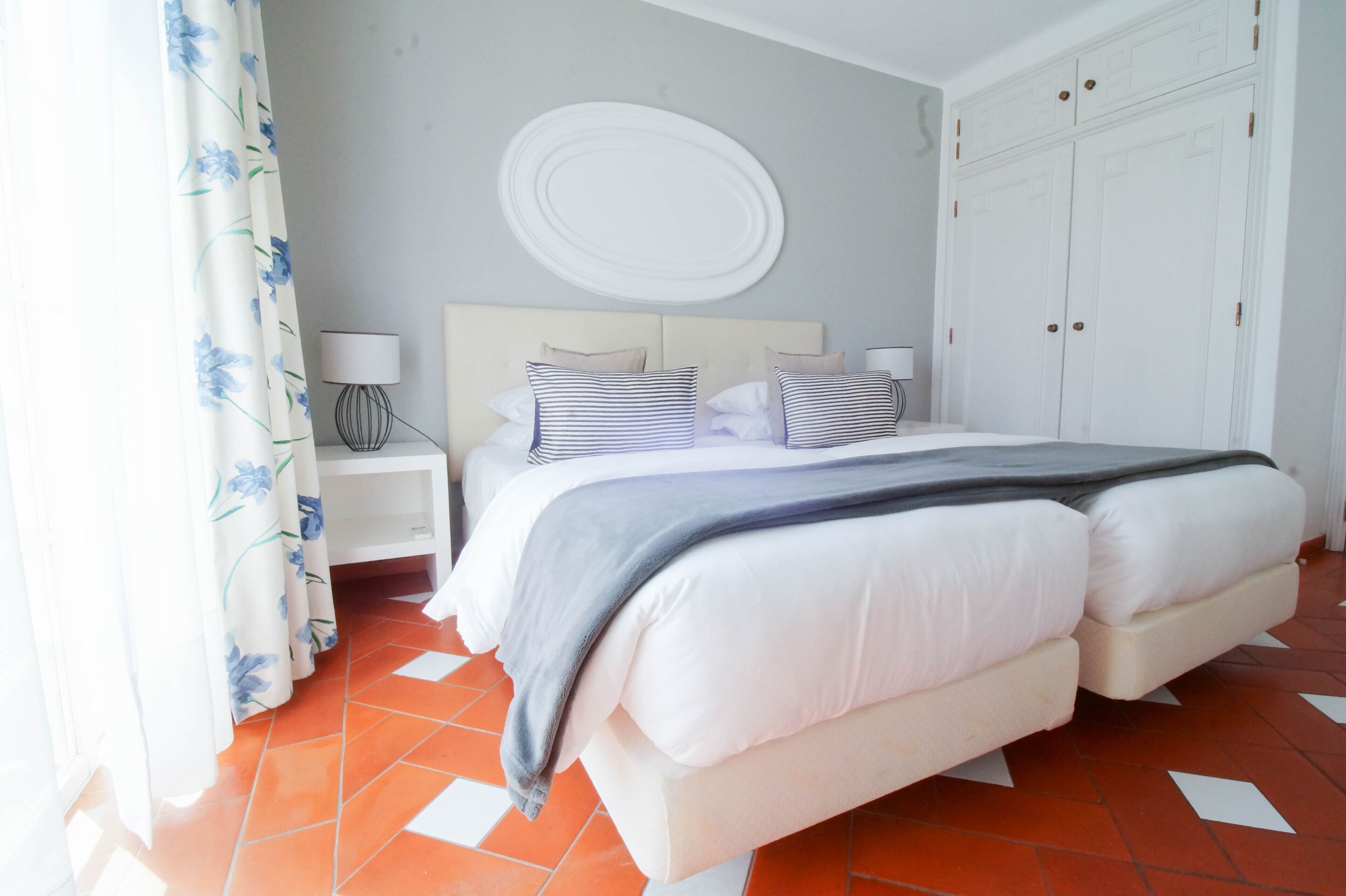 Une chambre à coucher avec un lit double, une tête de lit blanche, deux tables de chevet avec des lampes, un grand élément de décoration circulaire blanc fixé au mur et une armoire à deux portes.