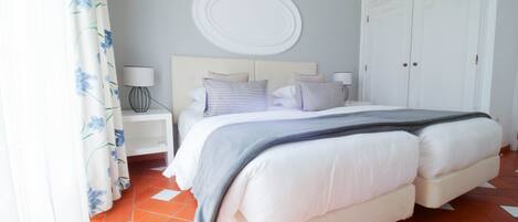 Une chambre à coucher avec un lit double, une tête de lit blanche, deux tables de chevet avec des lampes, un grand élément de décoration circulaire blanc fixé au mur et une armoire à deux portes.