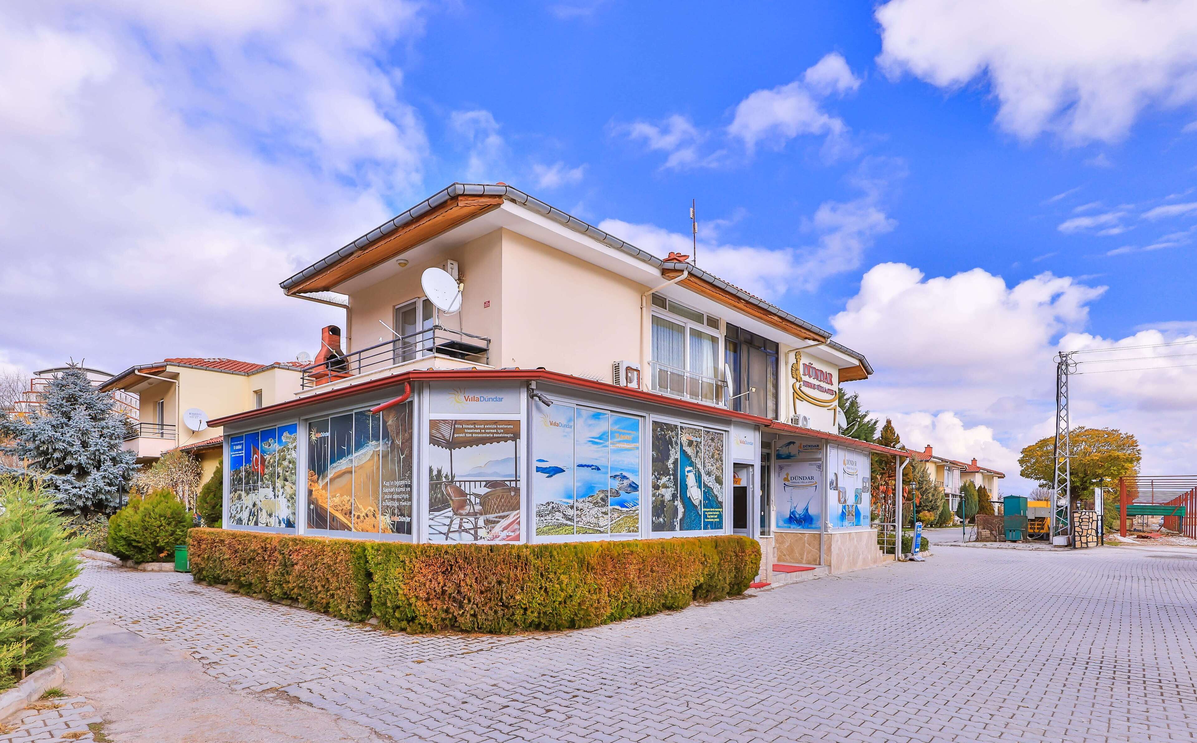 A building with a balcony, a sign for 'VillaDundar', and a paved area with a hedge.