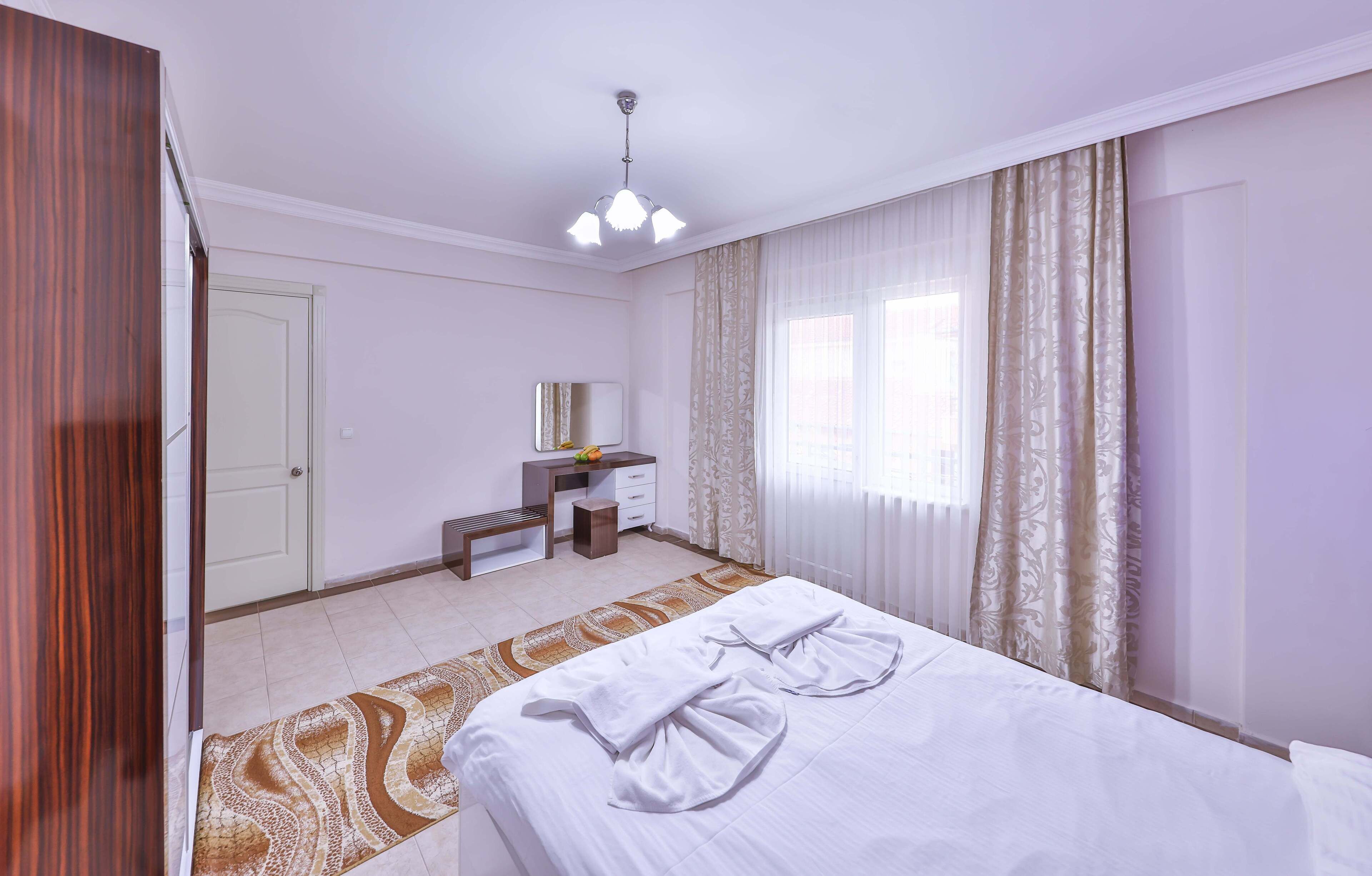 Une chambre d’hôtel avec un lit, un bureau, un miroir et une fenêtre avec des rideaux.