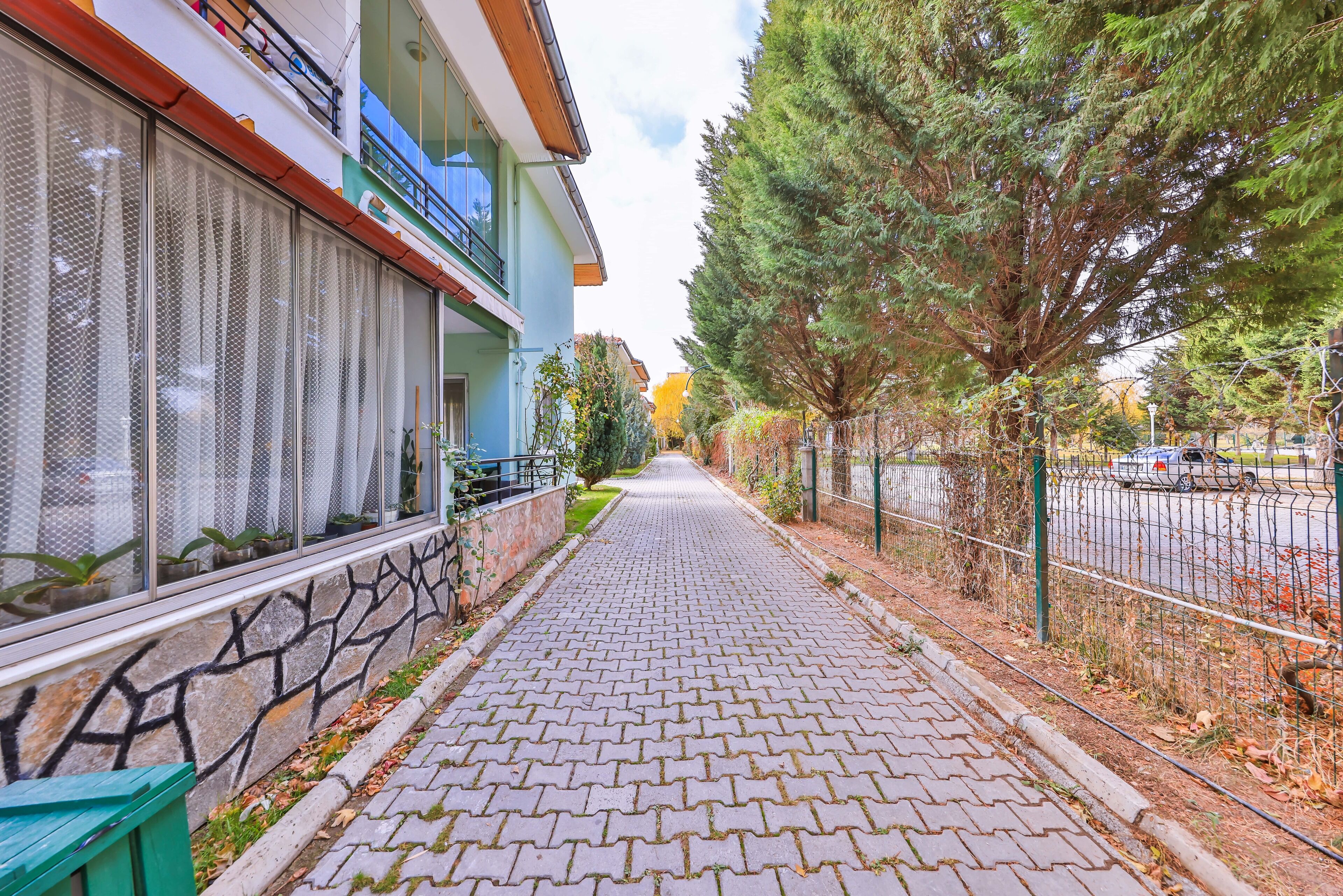 A paved pathway leading to a building with a balcony, a fence, and trees.