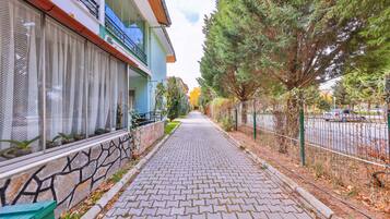 A paved pathway leading to a building with a balcony, a fence, and trees.
