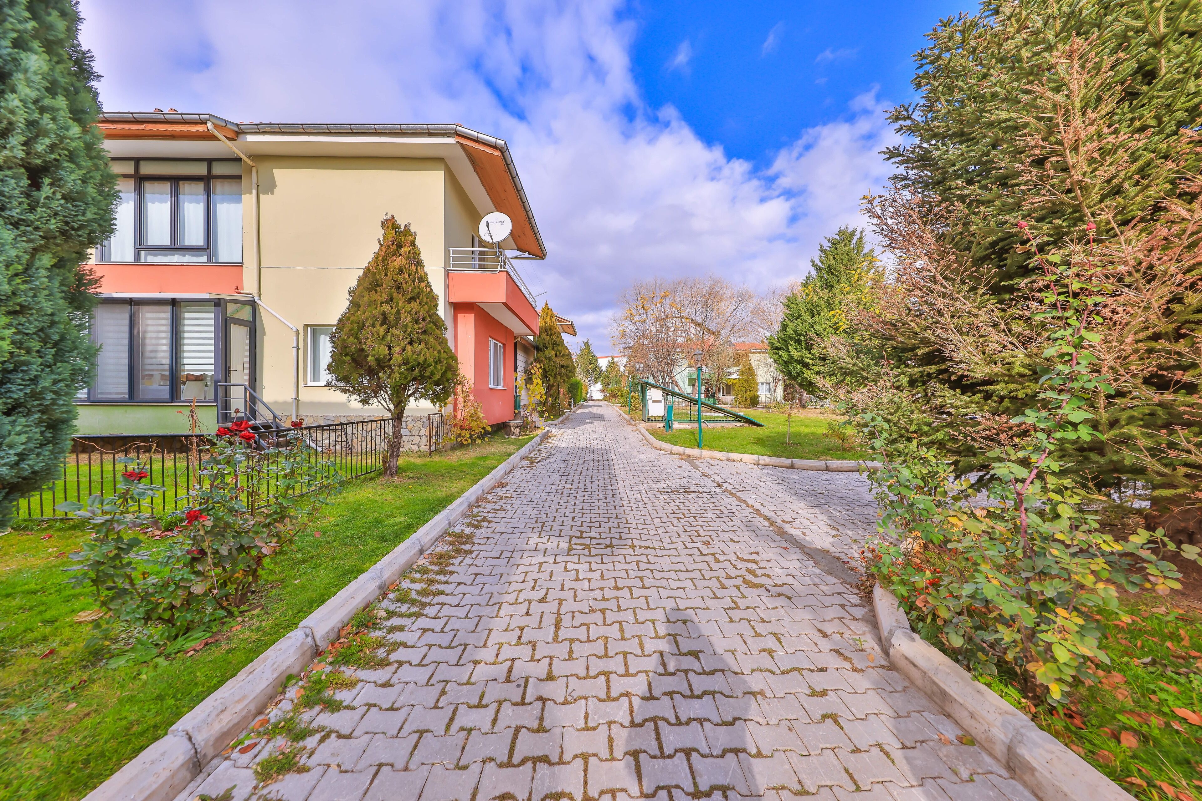 A paved pathway leading to a building with a balcony and a satellite dish.
