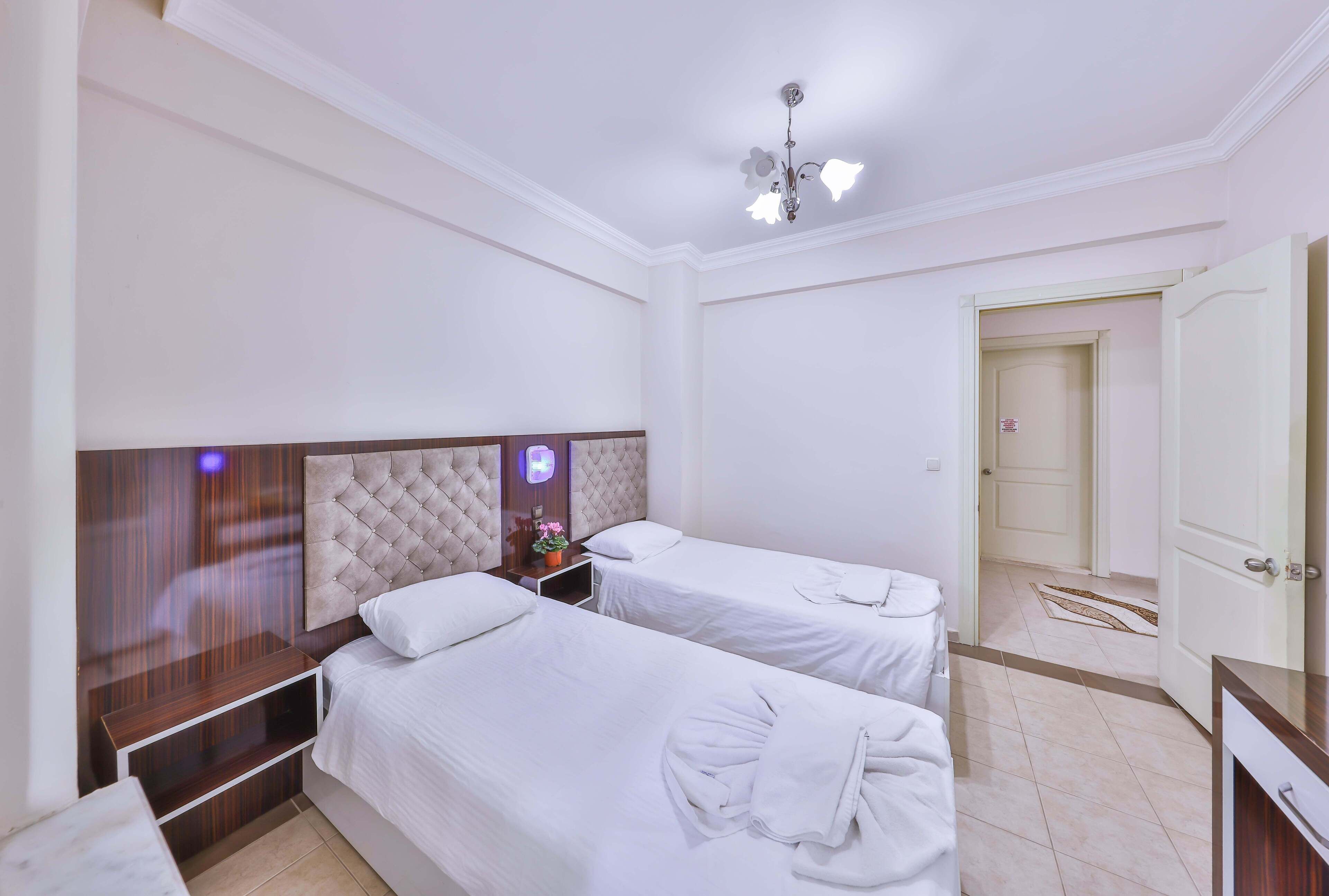 A hotel room with two beds, a wooden headboard, a bedside table with a lamp, and a door leading to another room.