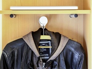 A black leather jacket hanging on a wooden hanger in a closet. - ibis budget Bayeux (Nonant)