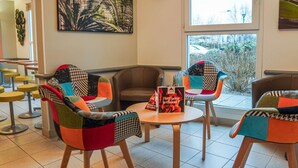 A modern interior with colorful chairs, a table, and a large window. - ibis budget Bayeux (Nonant)