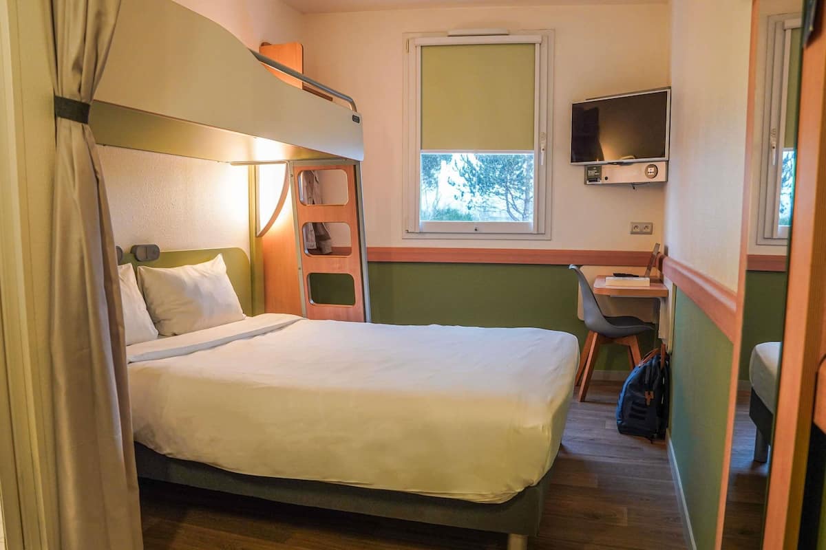 A single bed with a headboard, a desk with a chair, a television, and a window.