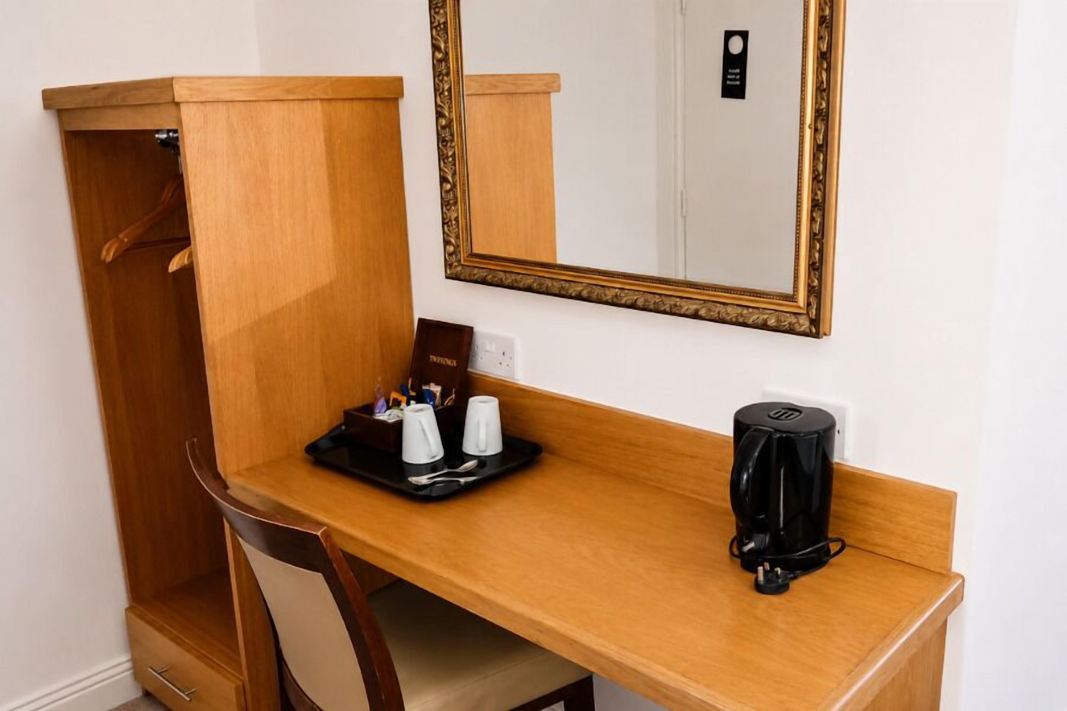 A wooden desk with a tray of toiletries, a black coffee maker, and a mirror with a gold frame.