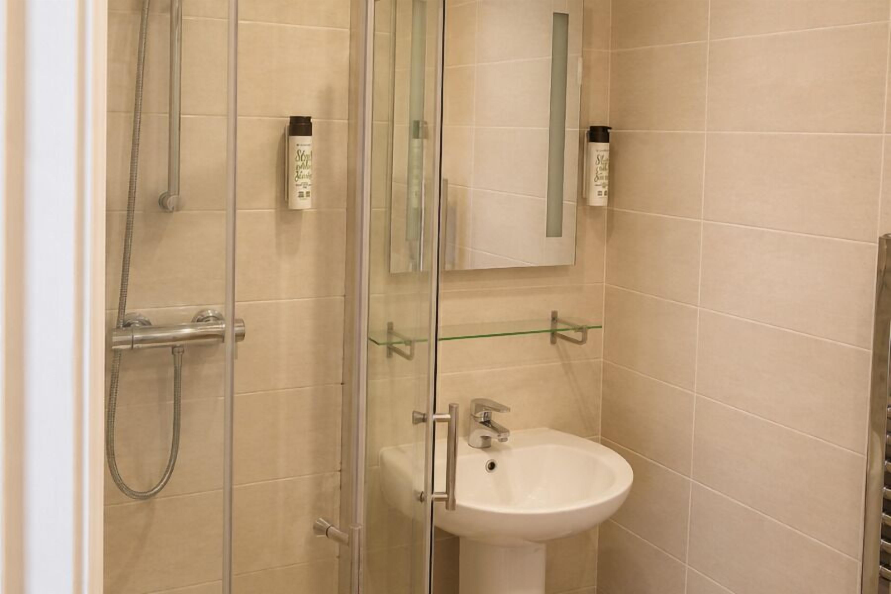 A bathroom with a glass shower enclosure, a white sink, and a mirror.