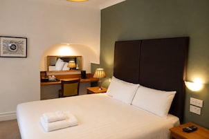 Una habitación de hotel con una cama, un escritorio, una silla, una lámpara y un espejo montado en la pared.