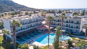 A hotel with multiple floors, a central pool area, and surrounding palm trees. - Dias Studios (Rhodes)