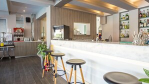 A modern bar area with a marble countertop, wooden stools, and a variety of bottles on shelves. - Dias Studios (Rhodes)