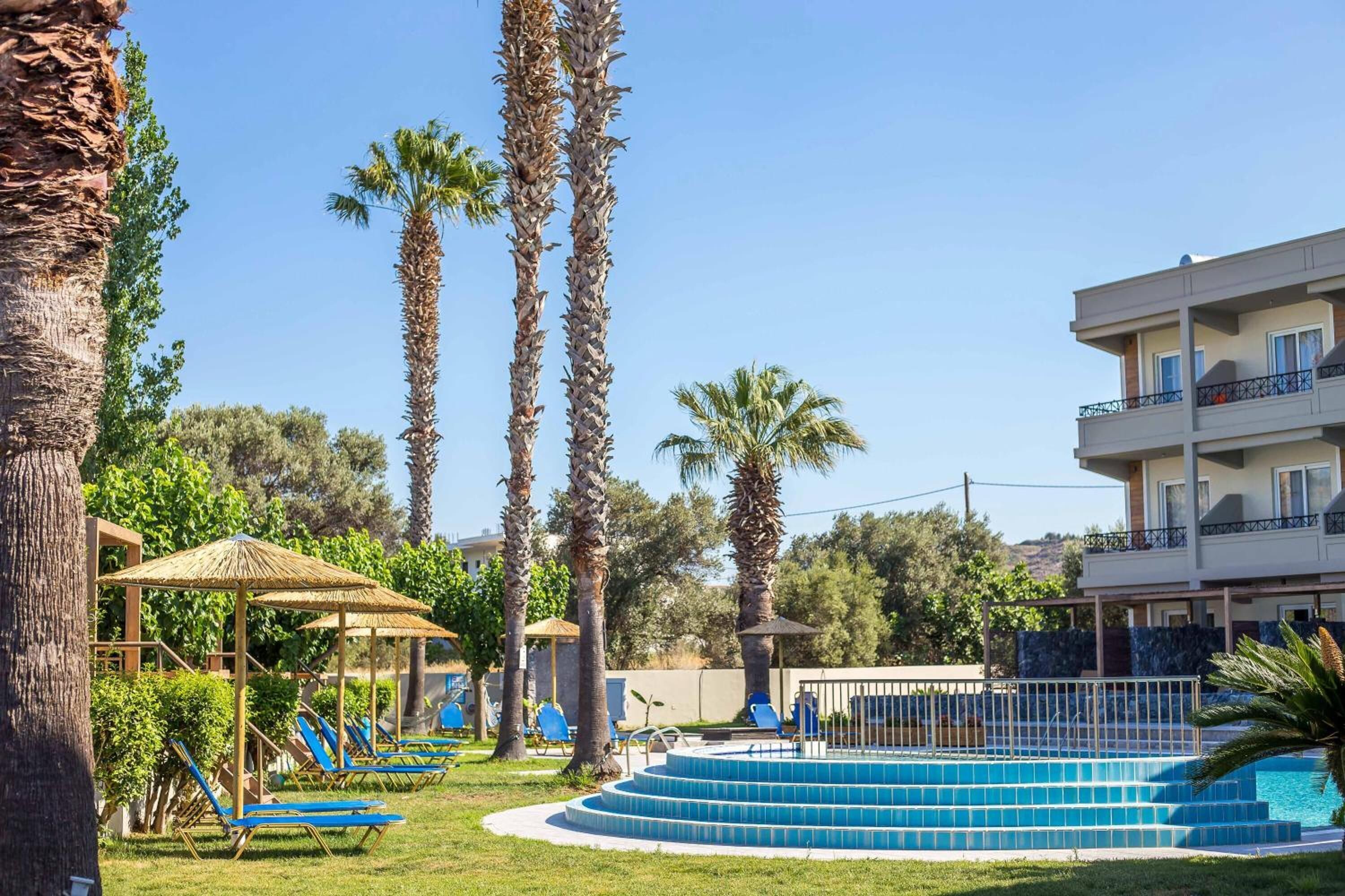 Uma área de piscina com espreguiçadeiras azuis, uma piscina circular e palmeiras.