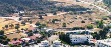 A coastal resort with multiple-story buildings, a central swimming pool, and a mountainous backdrop.