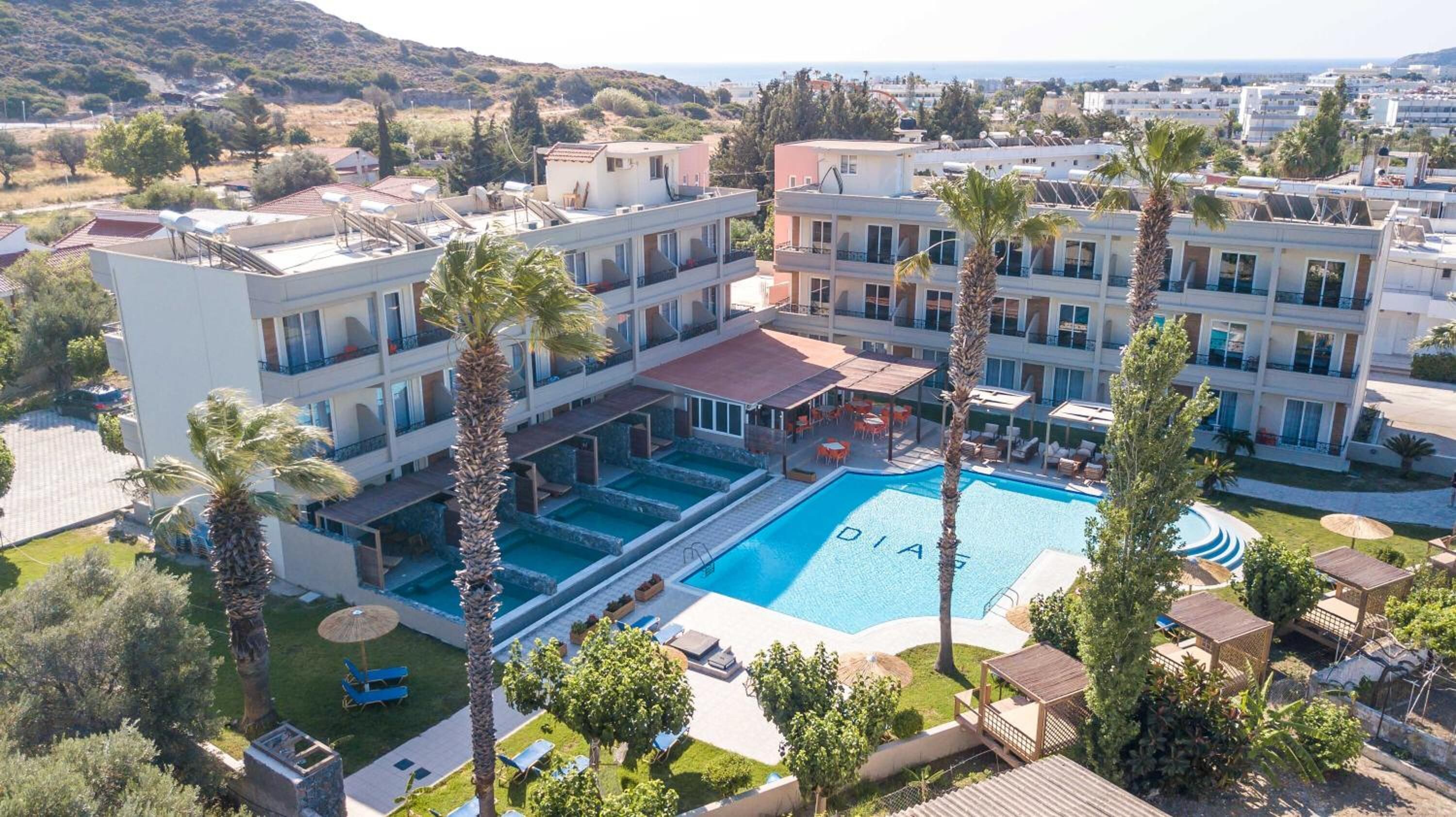 A hotel with a central swimming pool, multiple balconies, and surrounding greenery.