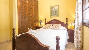 A bedroom with a wooden bed, a large wardrobe, a nightstand with lamps, and a floral curtain. - Las Mayoralas (Periana)
