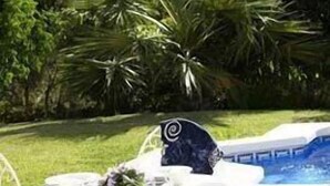 An outdoor dining area with a table set for two, a decorative item, and a view of a pool and mountains in the background. - Las Mayoralas (Periana)