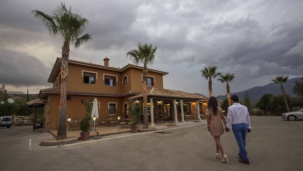 A two-story building with a patio area, palm trees, and a car parked nearby. - Las Mayoralas (Periana)