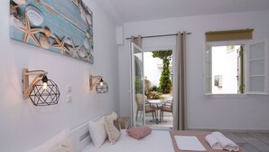 A bedroom with a bed, a sofa, a dining table, and a view of the outside. - Camara Hotel (Naxos)