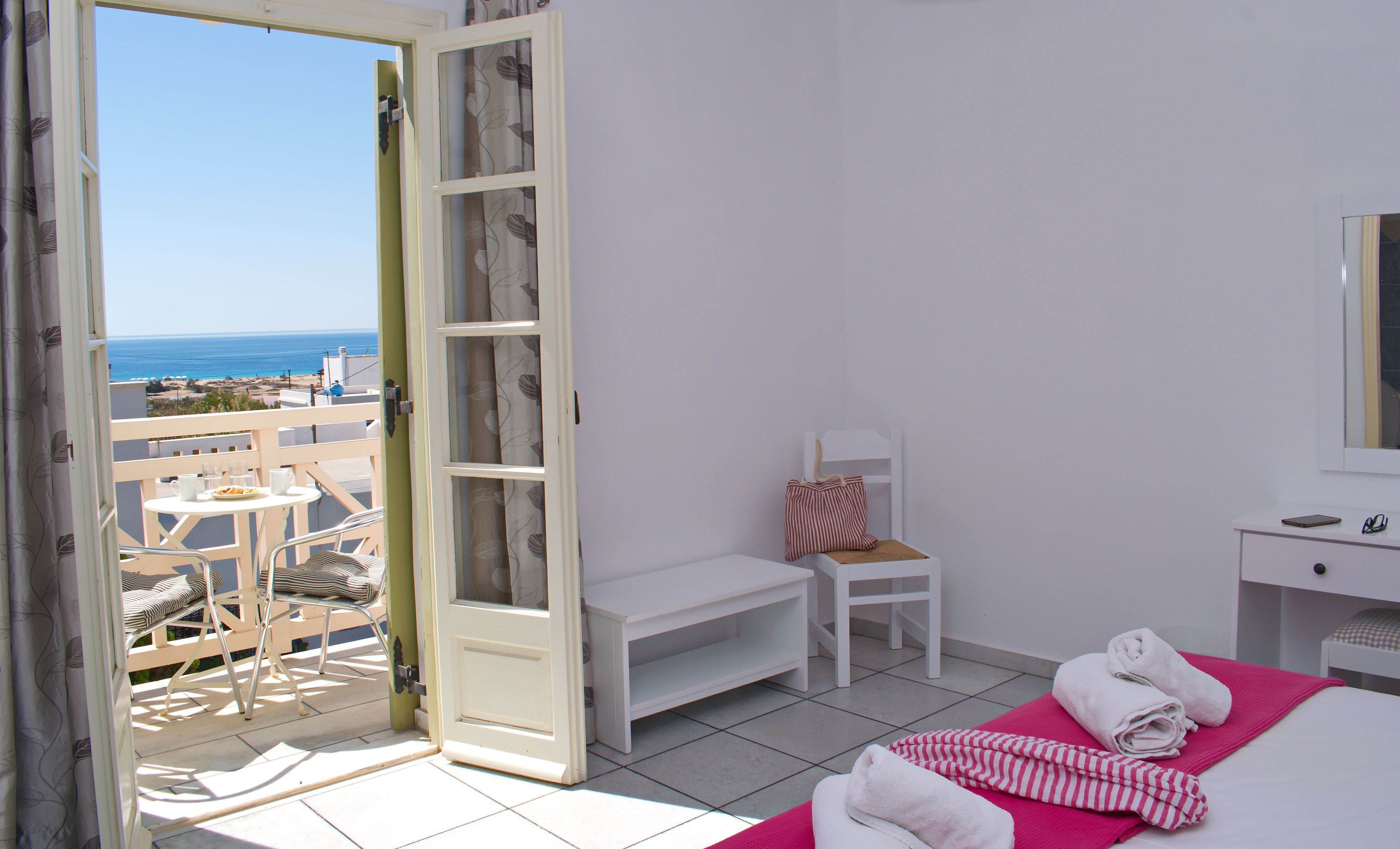 A hotel room with a balcony, a bed with towels, a chair, a small table, and a bedside table with a mirror.