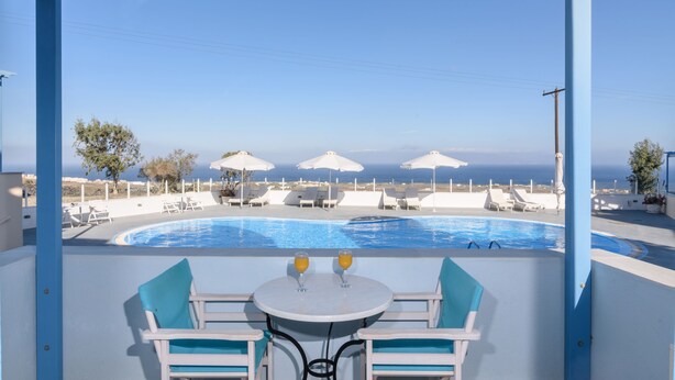 A poolside area with a table and chairs, umbrellas, and a view of the sea. - Maria's Place - Adults Only (Oia)