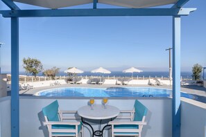Zona junto a la piscina con mesa y sillas, sombrillas y vista al mar.