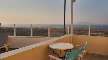 A balcony with a table and chairs, offering a view of a landscape with distant mountains and fields.
