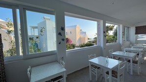 A bright room with large windows, white furniture, and a view of buildings outside. - Maria's Place - Adults Only (Oia)