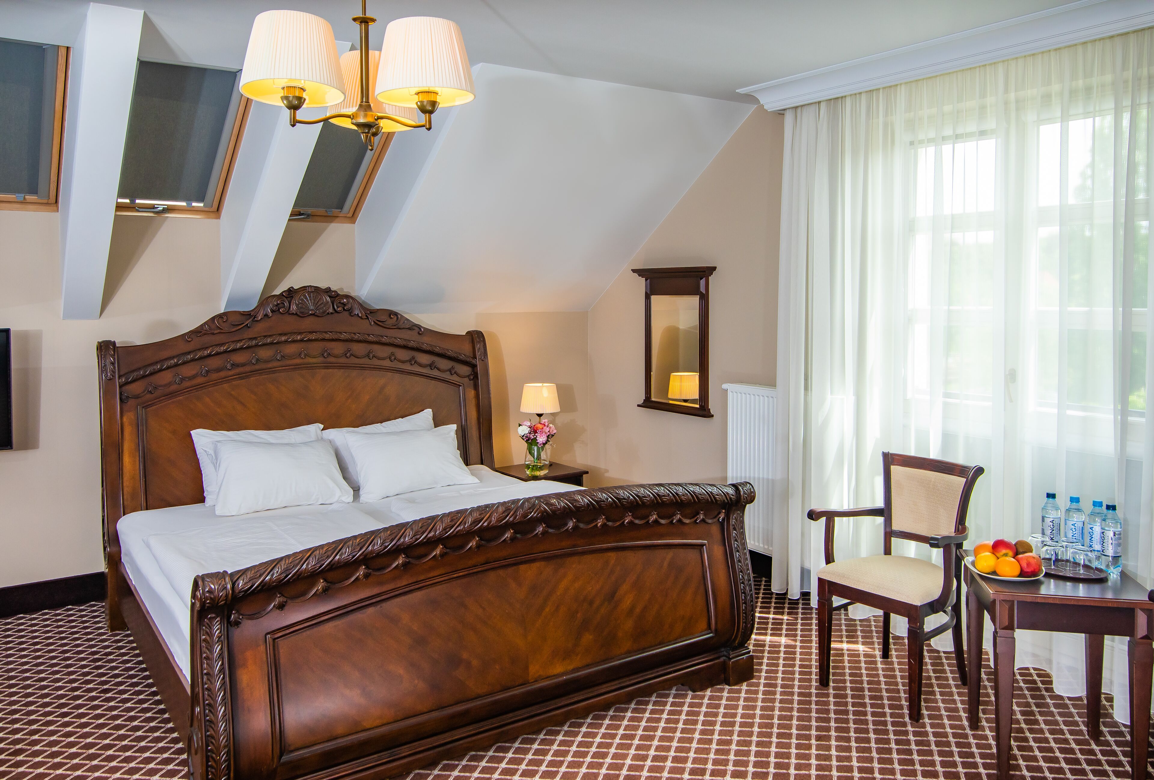 A hotel room with a large bed, a chair, a table with fruit, and a lamp.
