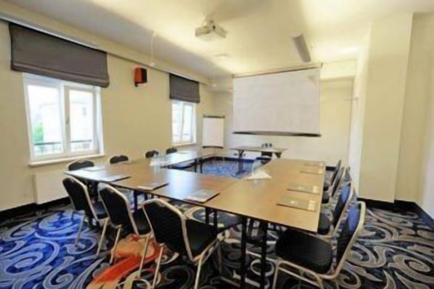 Una sala de conferencias con una gran mesa, sillas, una pantalla de proyector y una pizarra.