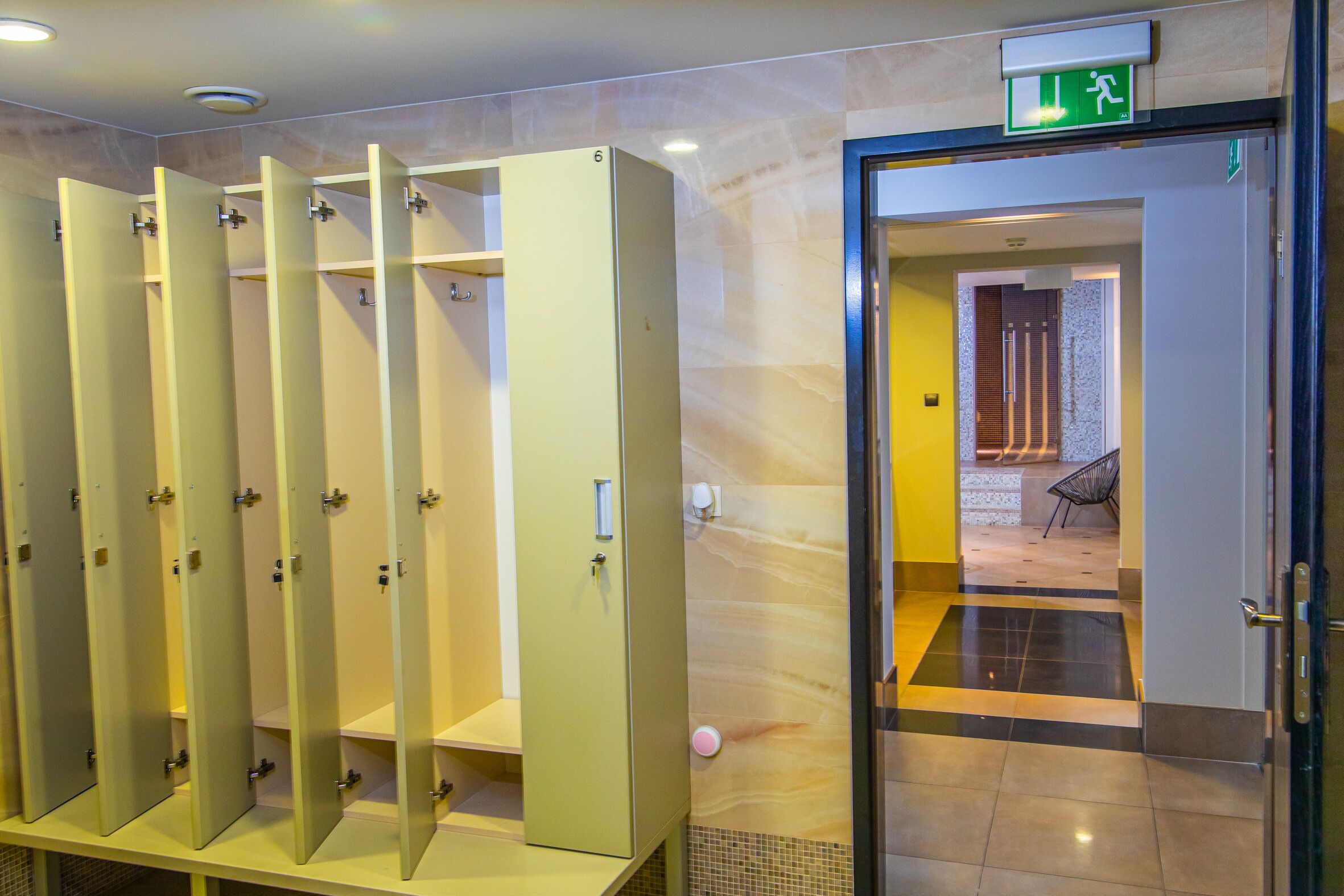 A row of individual lockers with a door and a green exit sign above.