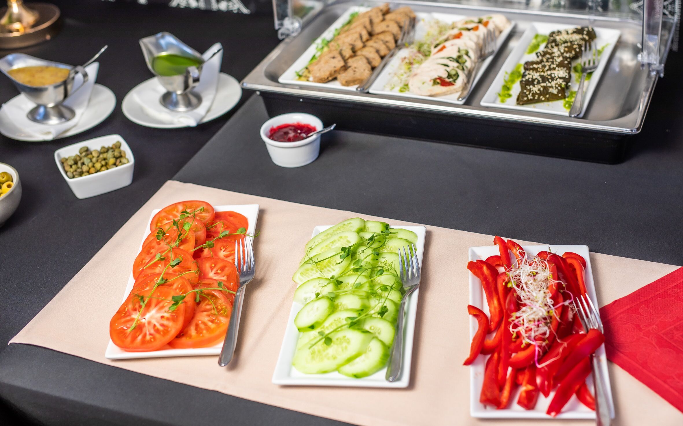 A buffet table with various food items including sliced tomatoes, cucumbers, and red bell peppers.