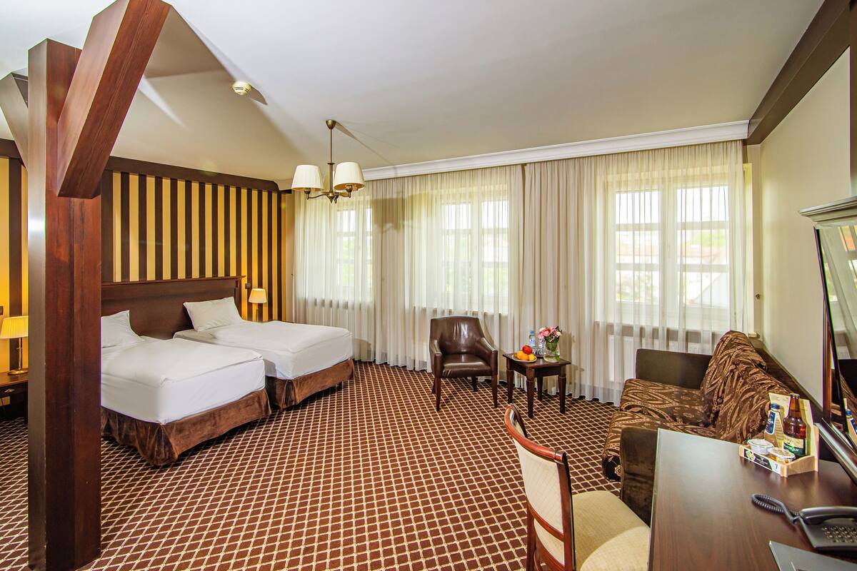 A hotel room with two beds, a sofa, a chair, a small table with a vase of flowers, and a desk with a telephone and a box of tissues.